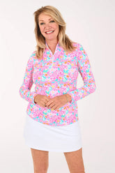 A woman modeling a long-sleeve collared top with a vibrant pink, blue, and orange floral pattern, paired with a white skirt, against a plain white studio background.