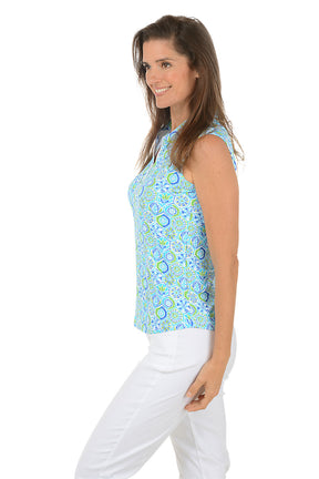 Woman wearing a sleeveless patterned top and white pants on a white background. Side shot.