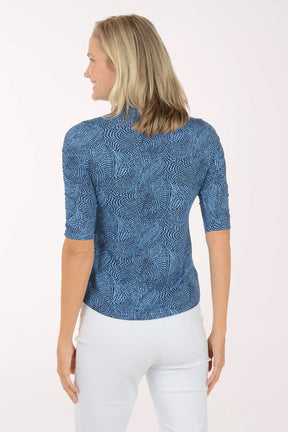 Woman wearing a blue patterned shirt with white pants on a white background