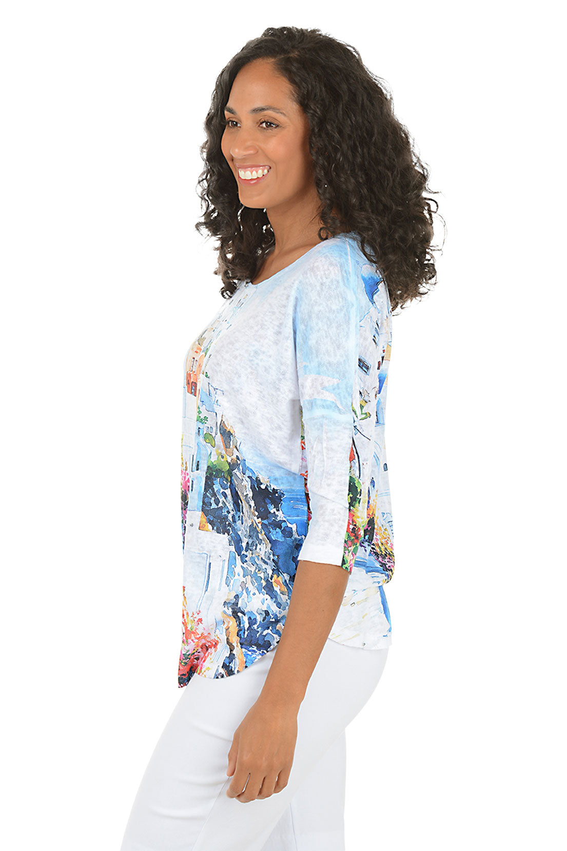 Woman wearing a colorful print top with a scenic design on a white background. Side shot.