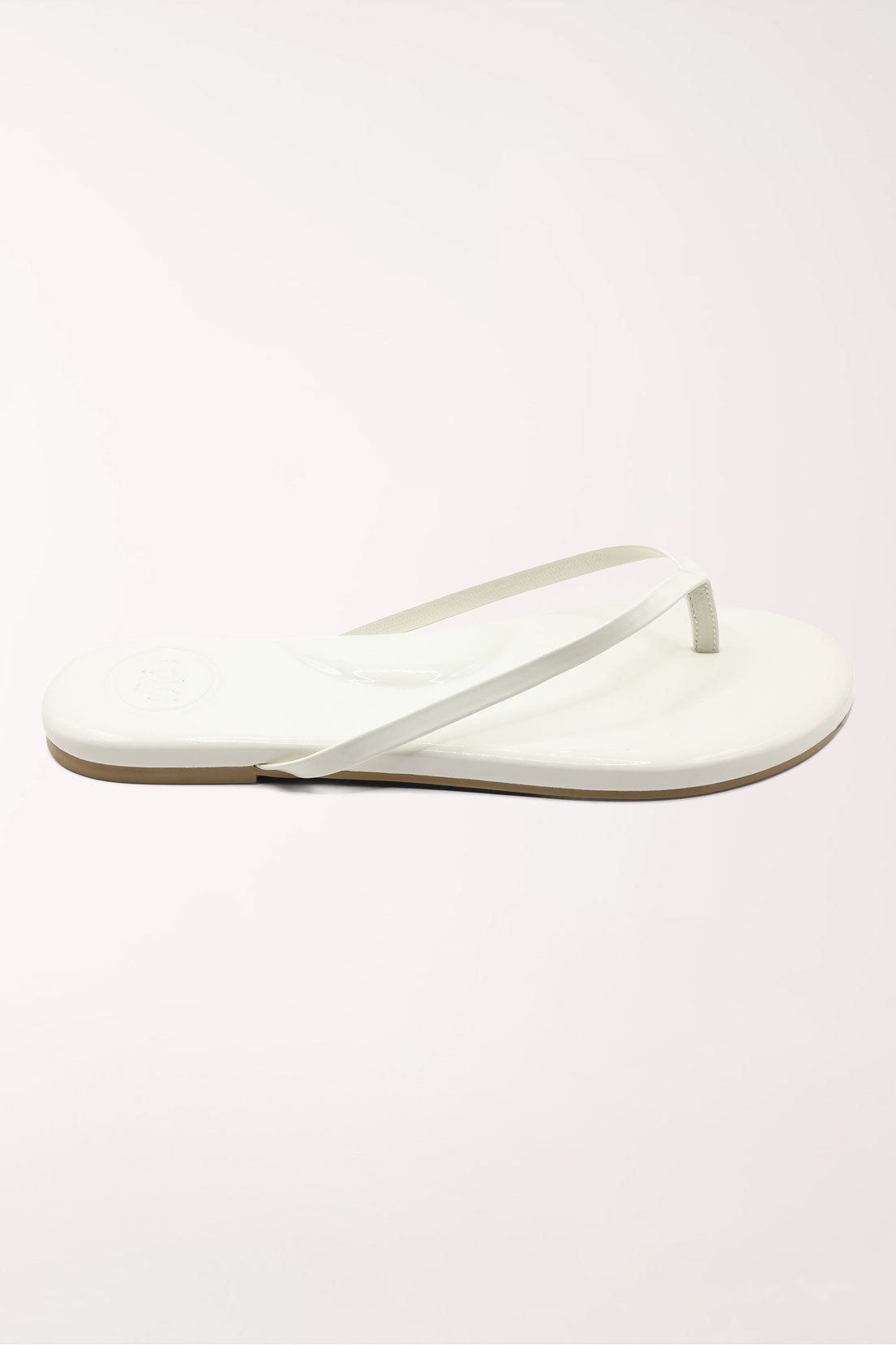 White flip-flop sandal with brown sole on a beige surface