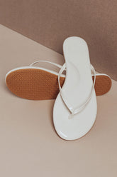 White flip-flop sandal with brown sole on a beige surface