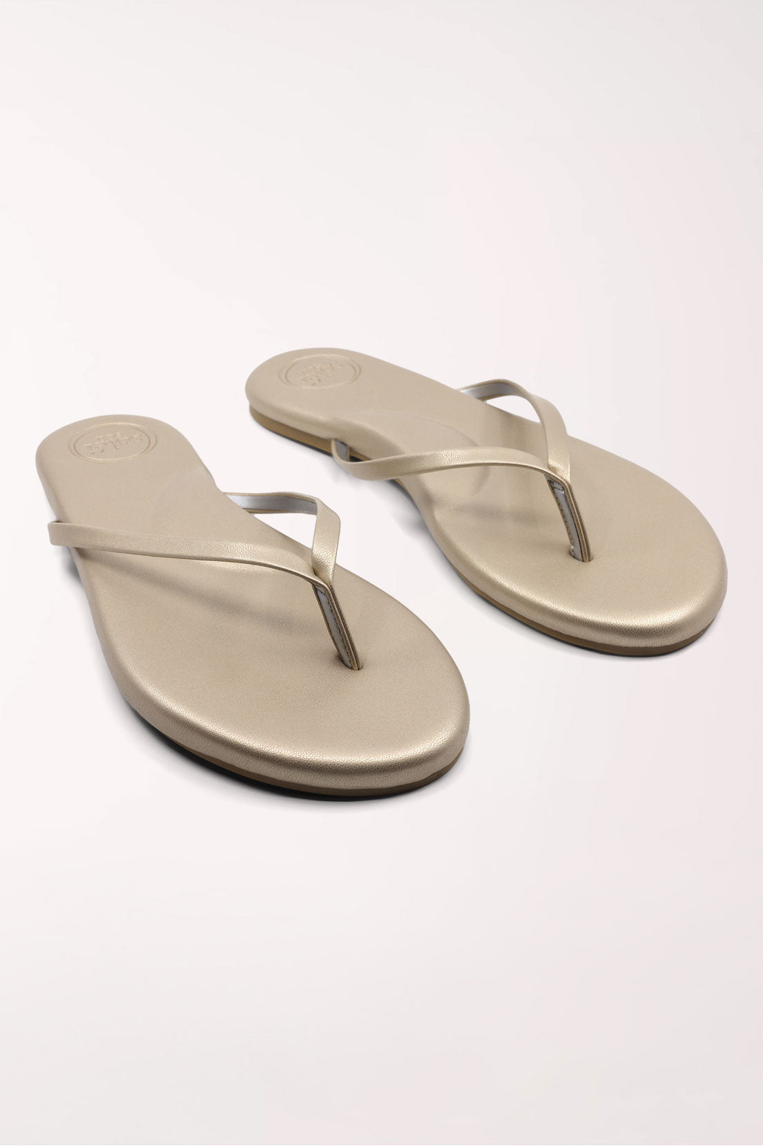 Pair of champagne gold flip-flops on a white background