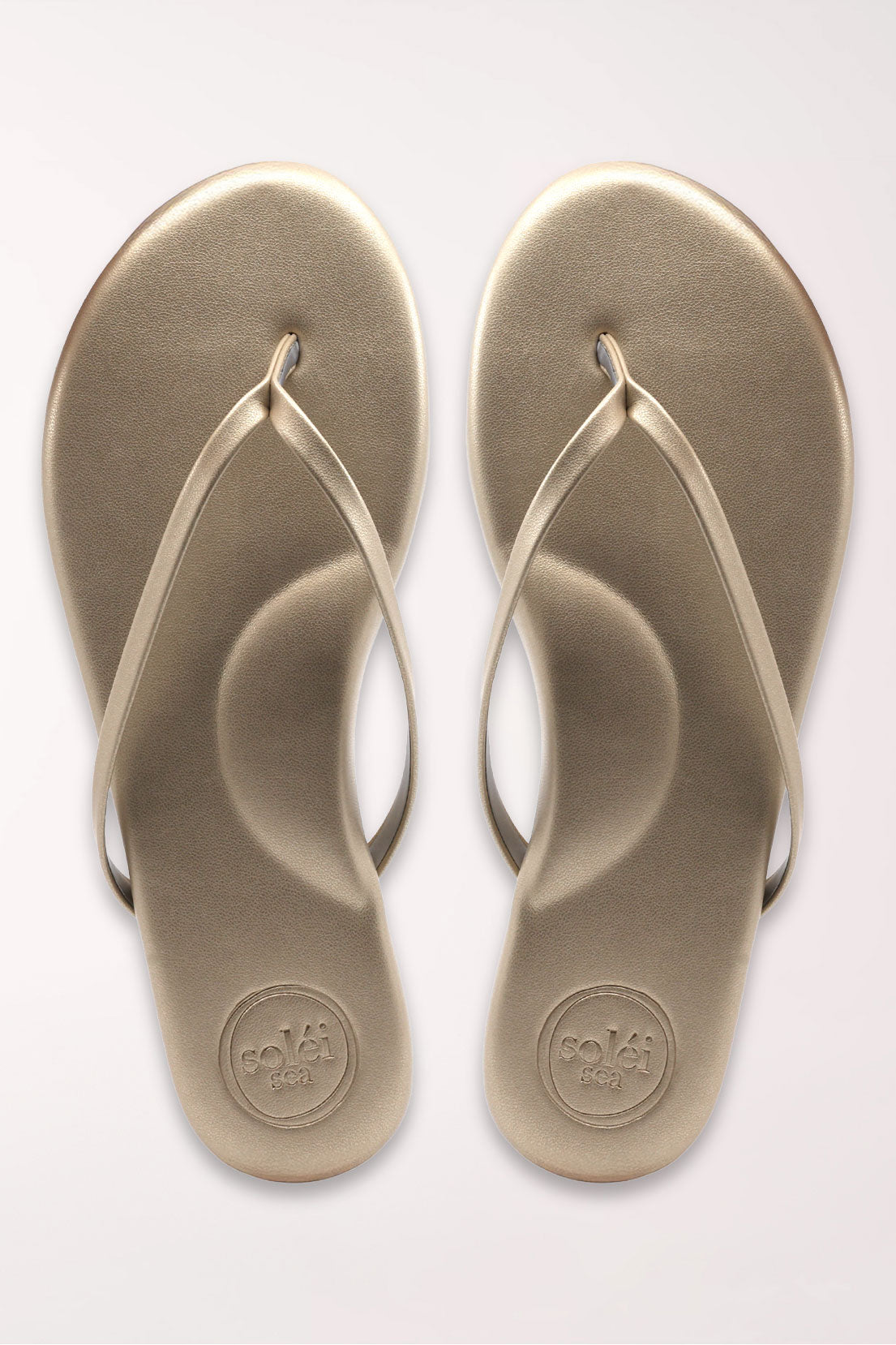 Pair of champagne gold flip-flops on a white background