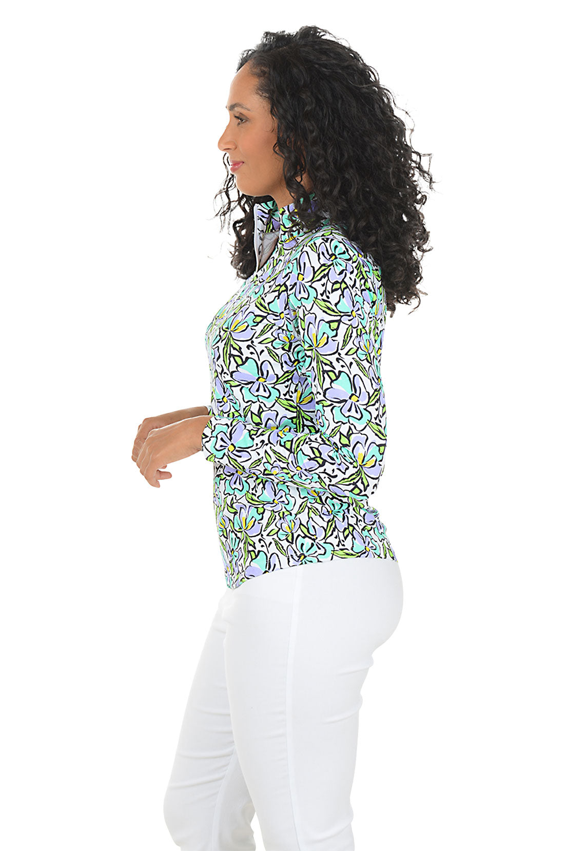 Woman wearing a colorful floral blouse with white pants on a white background. Side shot.
