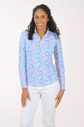 Woman wearing a colorful patterned blouse with white pants on a plain background
