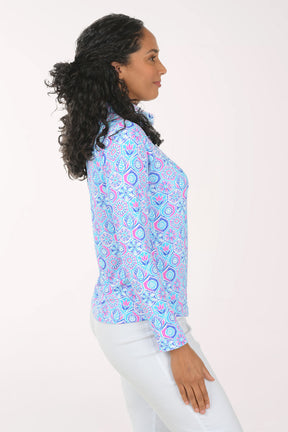 Woman wearing a colorful patterned blouse with white pants on a plain background