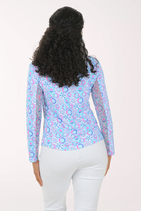Woman wearing a colorful patterned blouse with white pants on a plain background