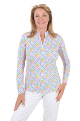Woman wearing a colorful patterned blouse with white pants on a white background.