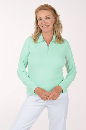 Woman wearing a light green long-sleeve shirt and white pants on a white background