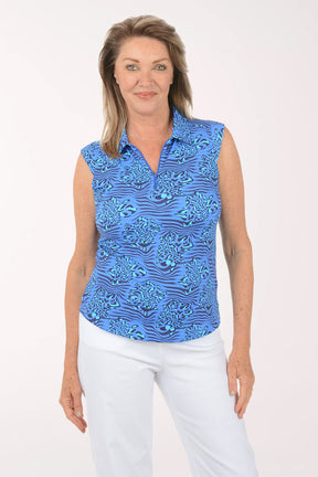 Woman wearing a blue patterned sleeveless top and white pants on a white background