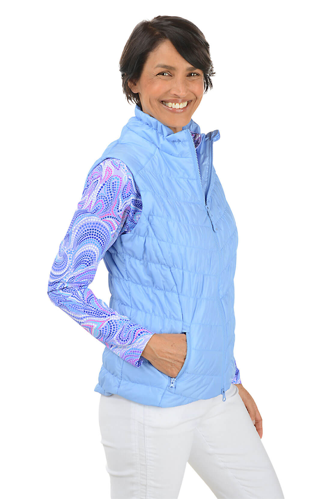 Woman wearing a light blue quilted vest with a colorful pattern on sleeves against a white background. Side shot.
