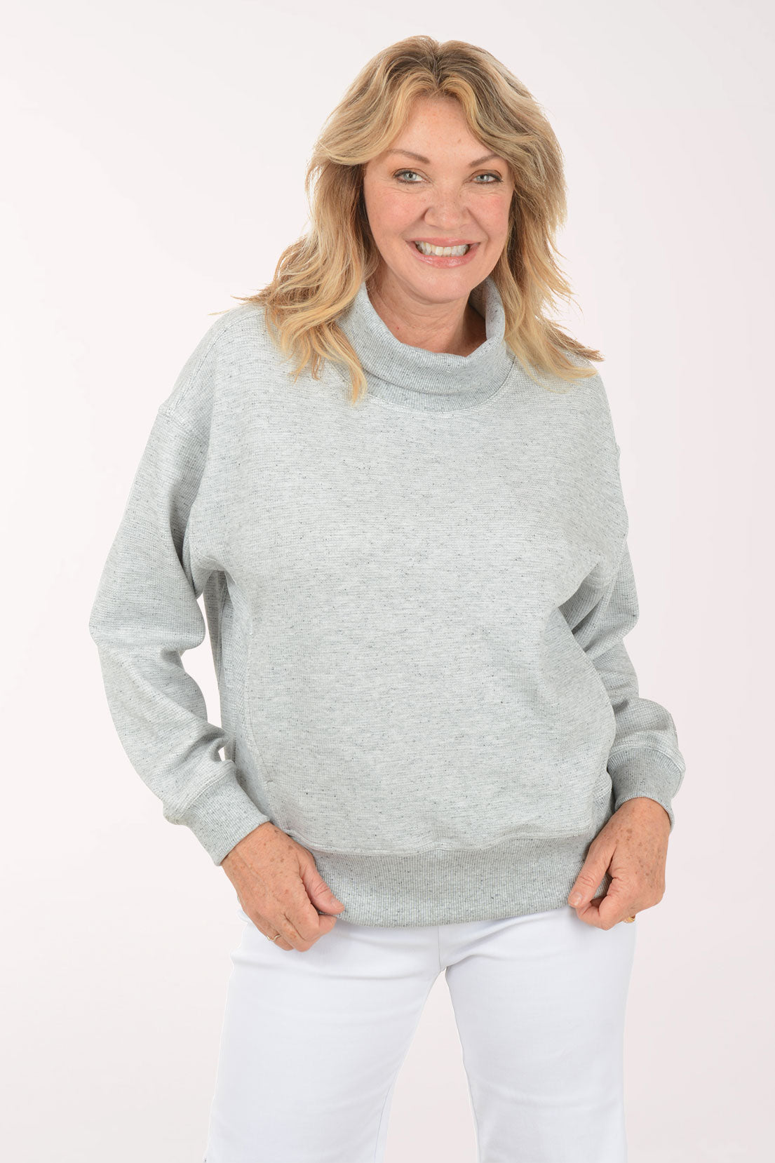 A woman wearing a grey funnel neck sweater.
