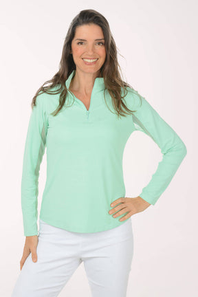 Woman wearing a light green long-sleeve shirt and white pants on a white background