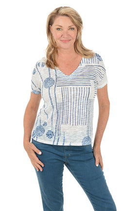 Woman wearing a white blouse with blue patterns and blue jeans on a white background.