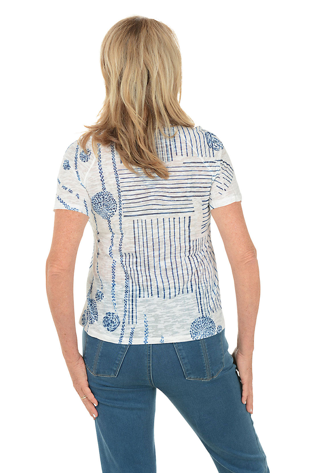 Woman wearing a white blouse with blue patterns and blue jeans on a white background. Back shot.