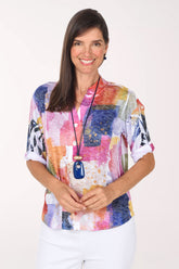 Model wearing the Impulse Prism Blocks High-Low Knit Top, a white burnout knit with watercolor blocks of pink, orange, yellow, purple and navy, front view