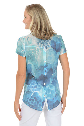 A woman wearing a blue v-neck short sleeve shirt with a button detail. Back shot.