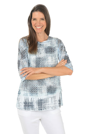 A woman wearing a 3/4 sleeve grey and white top with an abstract square pattern.