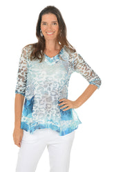 Woman wearing a patterned blue and white blouse with white pants on a white background.