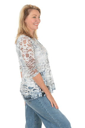 Woman wearing a patterned blouse with sheer sleeves on a white background. Side shot.