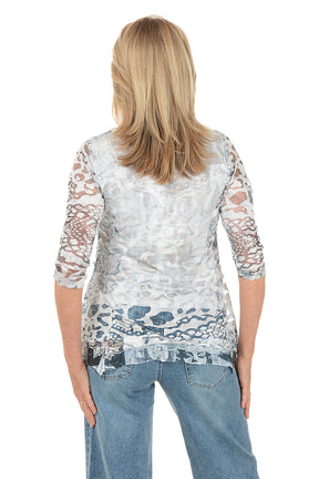 Woman wearing a patterned blouse with sheer sleeves on a white background. Back shot.