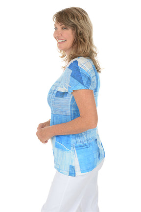 A woman wearing a blue short sleeve top with a blue and white abstract pattern. Side shot.