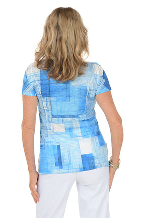A woman wearing a blue short sleeve top with a blue and white abstract pattern. Back shot.