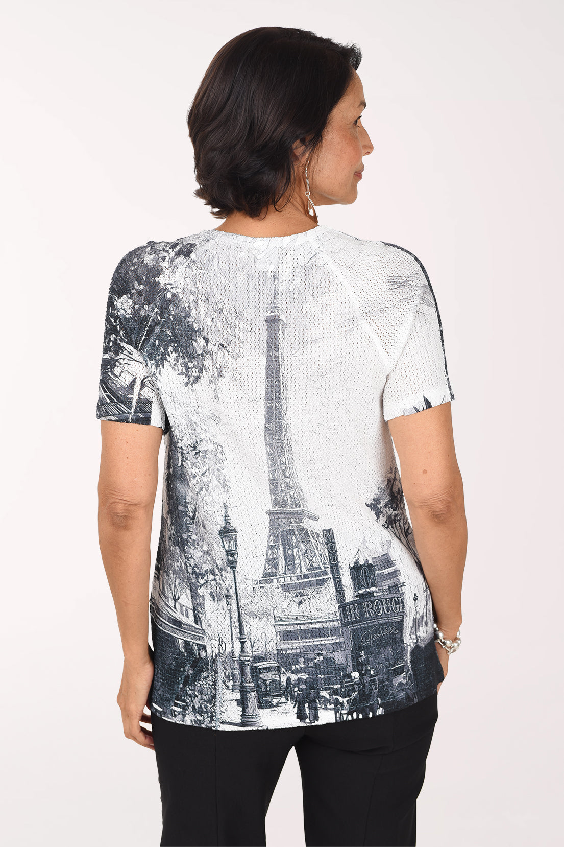 Back view of the white eyelet top showing the Paris street scene with the Eiffel Tower continuing across the back, worn with black pants.
