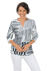 Woman wearing a 3/4 sleeve black and white patterned blouse with white pants on a white background.
