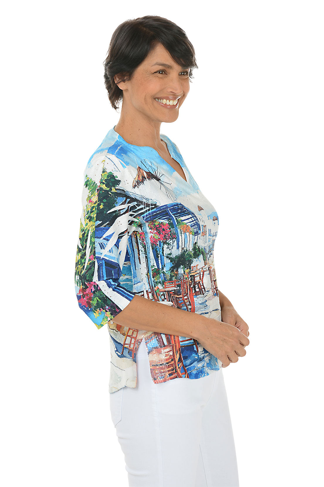 Woman wearing a 3/4 sleeve colorful beach-themed shirt with a scenic print. Side shot.