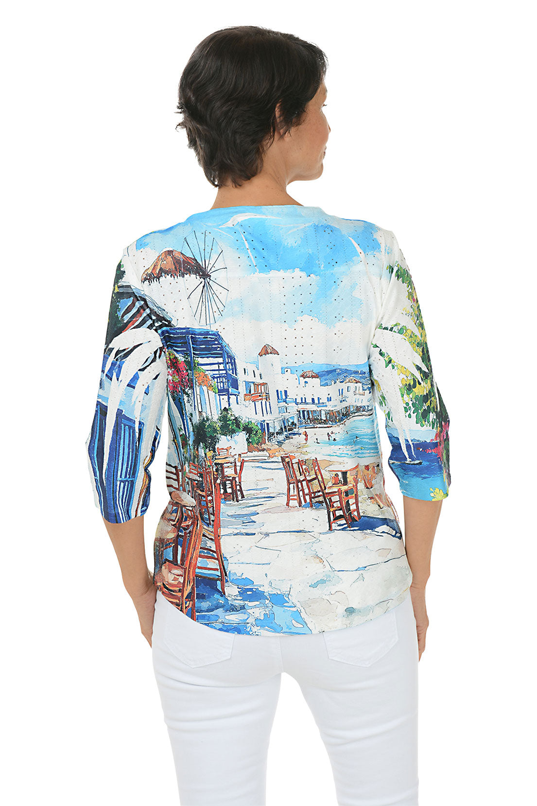 Woman wearing a 3/4 sleeve colorful beach-themed shirt with a scenic print. Back shot.