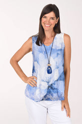 Model wearing the Impulse Porcelain Garden Eyelet Sleeveless Top, white eyelet with large cornflower blue watercolor blooms, with a blue pendant necklace, front view