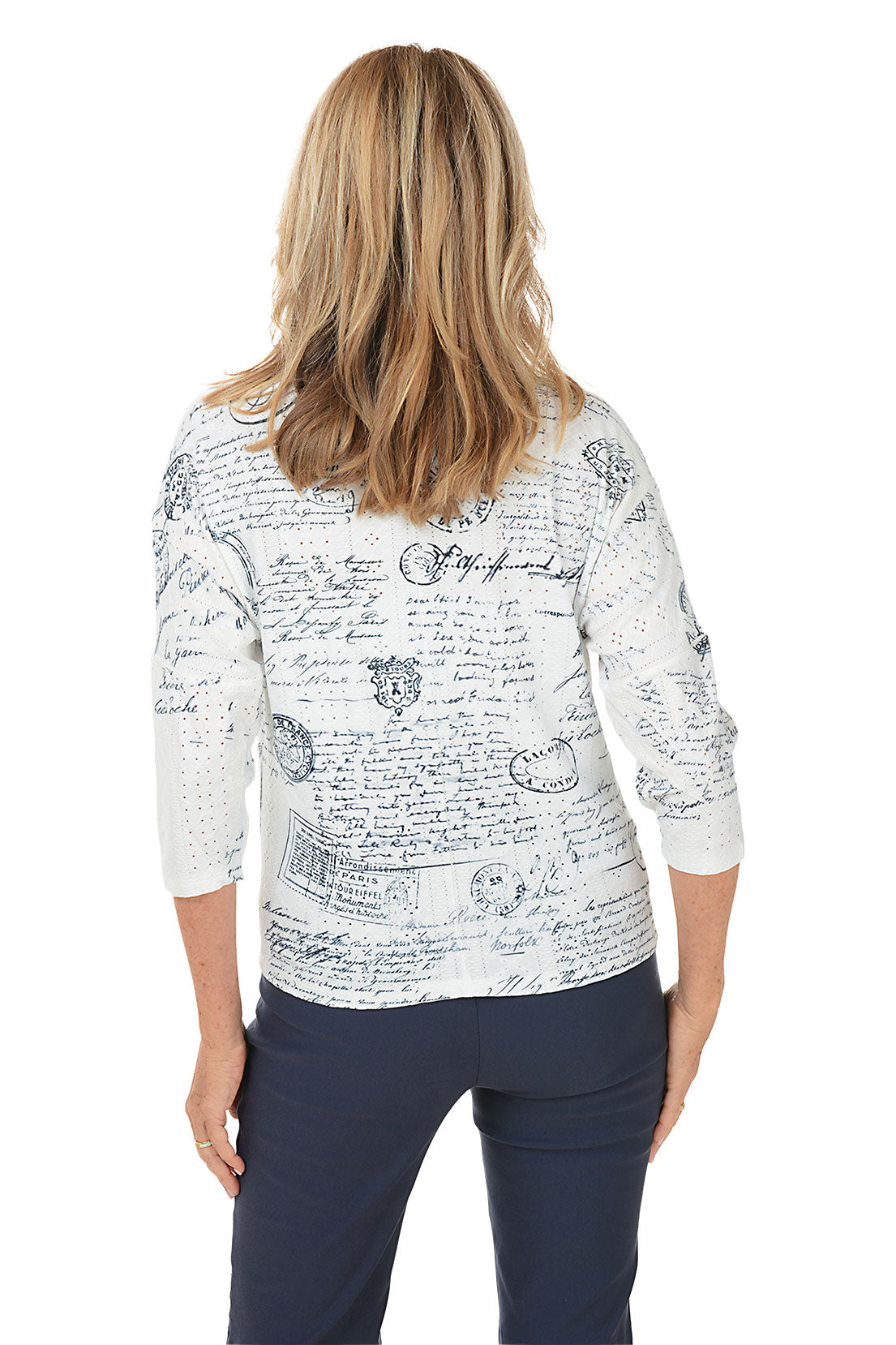 Woman wearing a white blouse with black text and graphics, standing against a white background. Back shot.