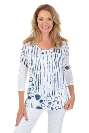 Woman wearing a white top with blue abstract patterns on a white background.