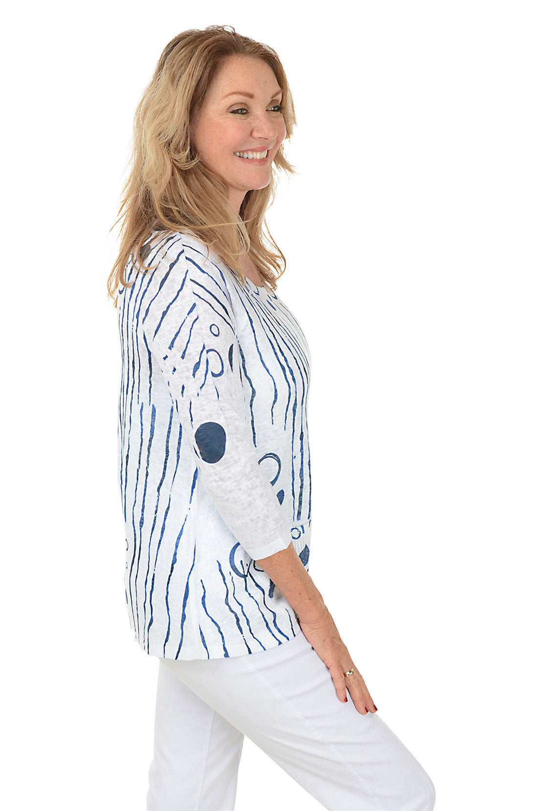 Woman wearing a white top with blue abstract patterns on a white background. Side shot.