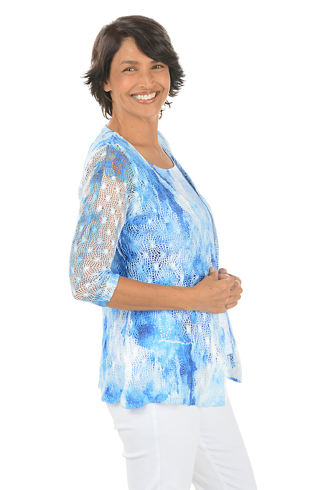 Woman wearing a blue and white patterned top with matching sweater with a plain background. Side shot.