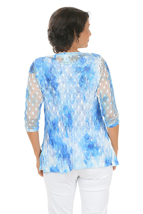 Woman wearing a blue and white patterned top with matching sweater with a plain background. Back shot.