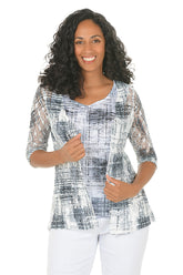 Woman wearing a patterned top with matching sweater and white pants on a white background.