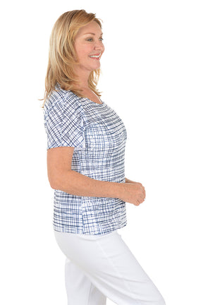 Woman wearing a blue checkered top and white pants on a white background. Side shot.
