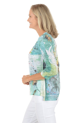 A woman wearing a 3/4 sleeve multicolored top with a sunflower pattern. Side shot.