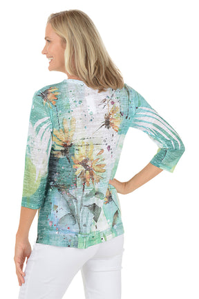 A woman wearing a 3/4 sleeve multicolored top with a sunflower pattern. Back shot.