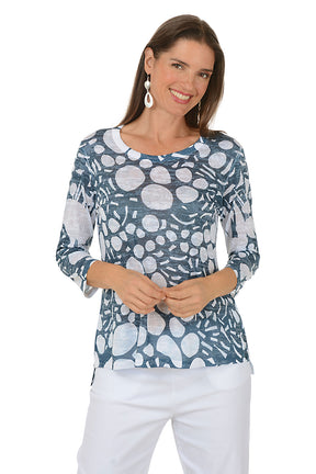 Woman wearing a blue floral patterned top with white pants on a white background.