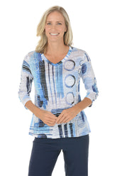 A woman wearing a v-neck 3/4 sleeve blue and white top with an abstract pattern.