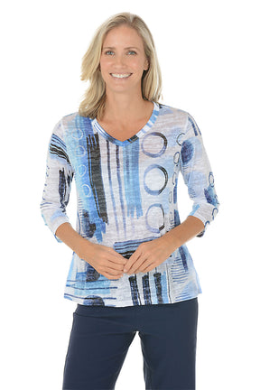 A woman wearing a v-neck 3/4 sleeve blue and white top with an abstract pattern.
