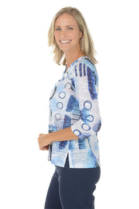 A woman wearing a v-neck 3/4 sleeve blue and white top with an abstract pattern. Side shot.