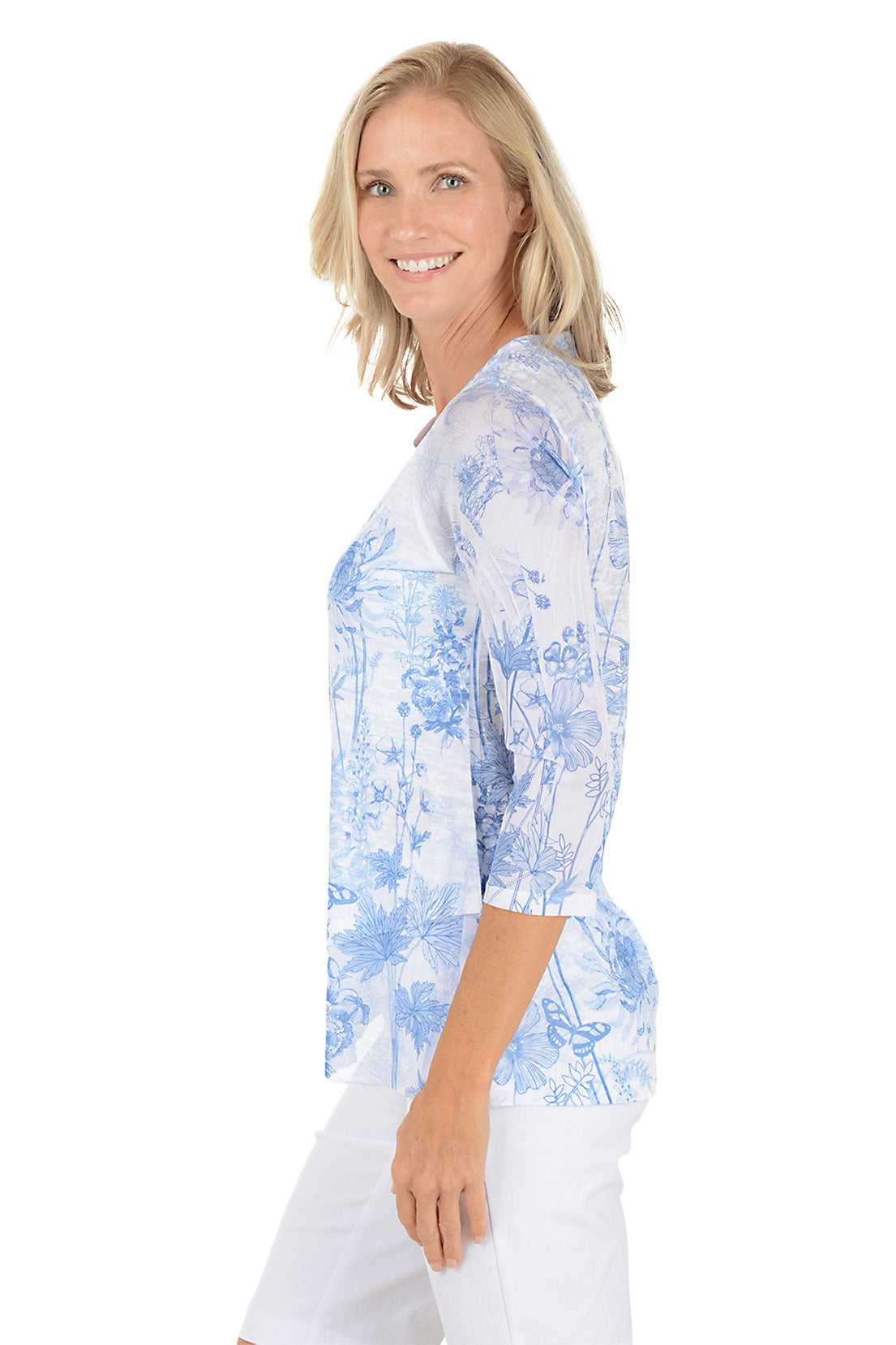A woman wearing 3/4 sleeve white and blue top with a floral pattern. Side shot.