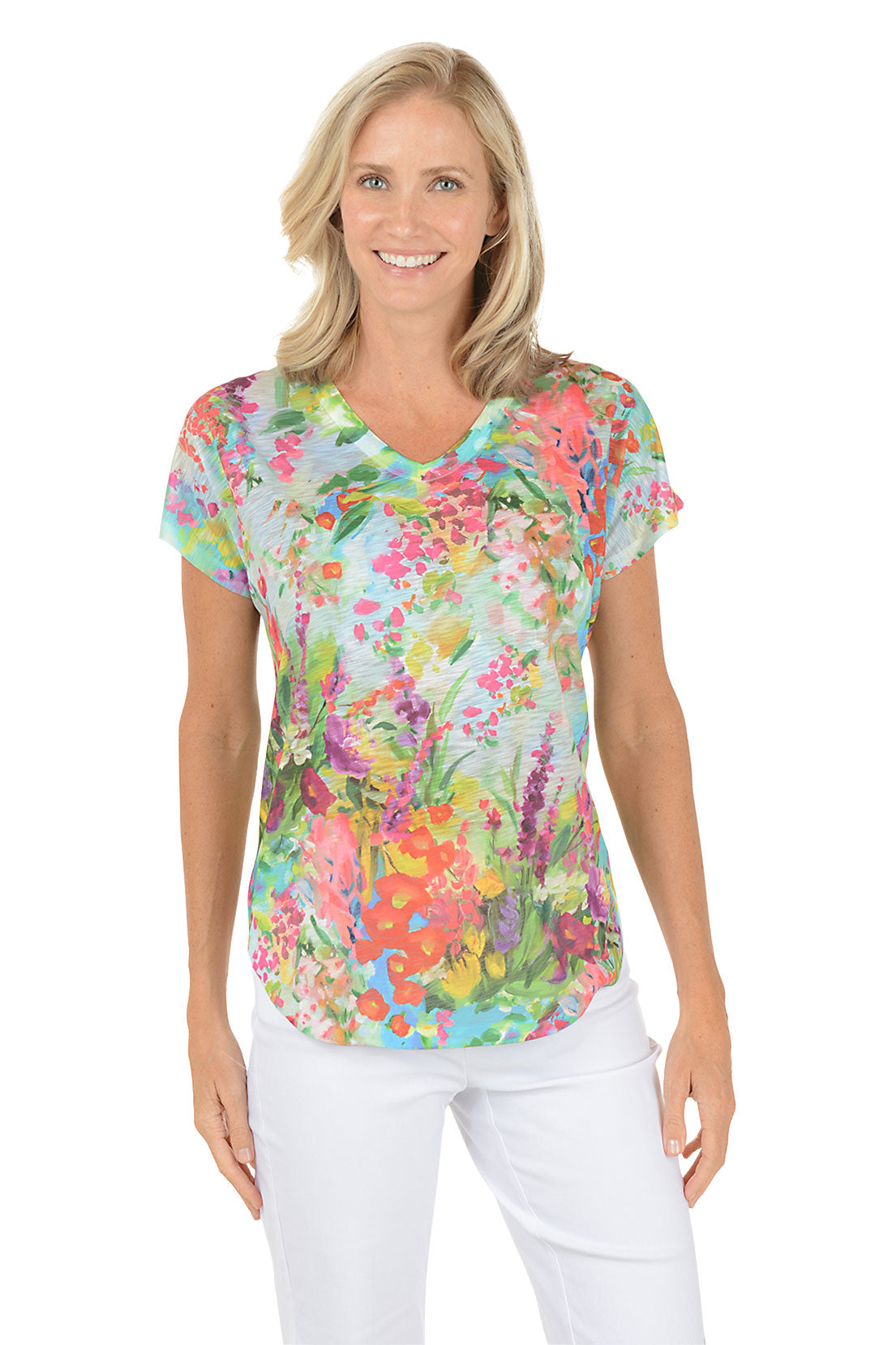 Woman wearing a colorful floral blouse with white pants on a white background. Second front shot.