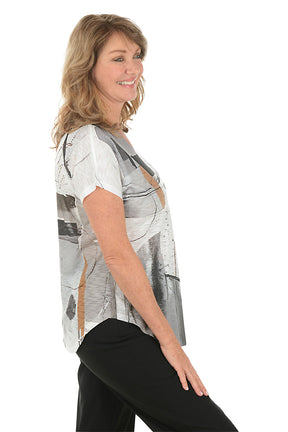 A woman wearing a black and white short sleeve v-neck shirt with an abstract design. Side shot.