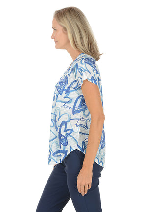 Woman wearing a blue and white patterned top on a white background. Side shot.